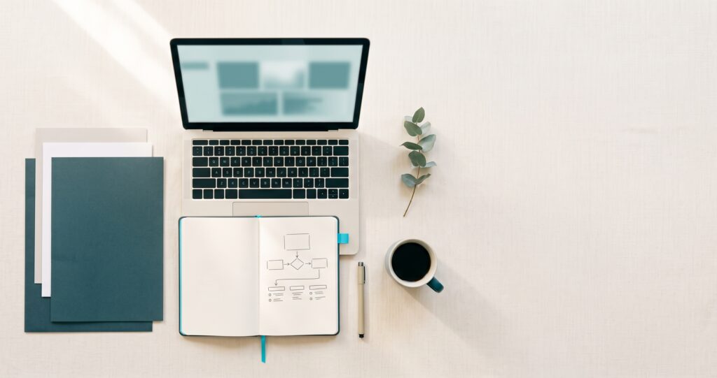 Overhead view of an organized desk with a laptop, notebook of checklists, documents, and coffee arranged neatly on a linen surface.